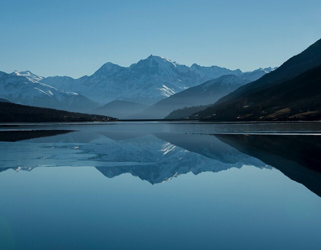 Snow-capped mountains reflected in a calm alpine lake Mountain lake reflecting snow-capped peaks under blue sky